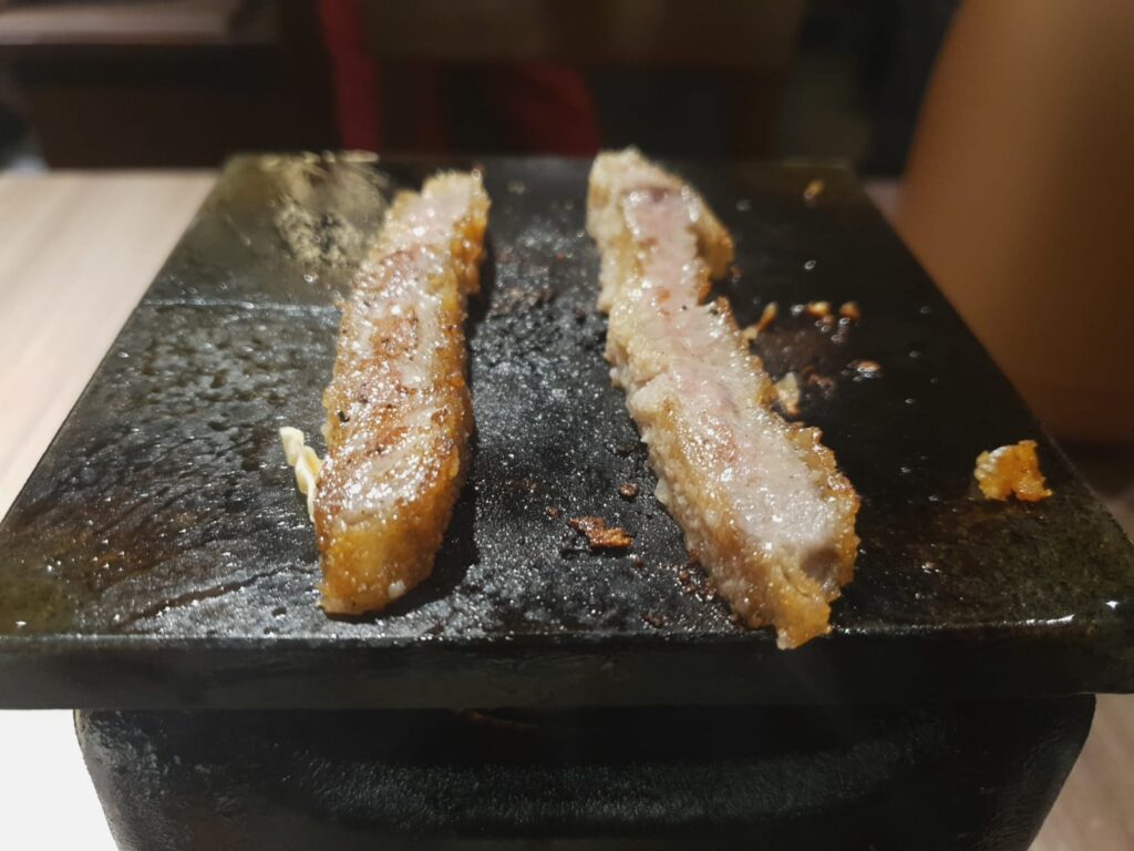 two cooked pieces of gyukatsu on hot stone